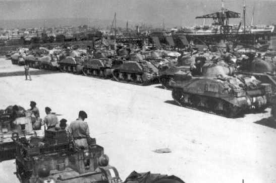 Carriers and Shermans waiting Pto embark at Catania for Italy. Note the different types of Shermans in the background.
